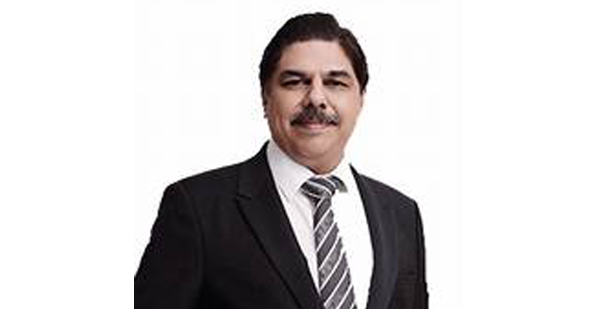 Professional man in a black suit and striped tie, smiling, against a white background (business portrait).